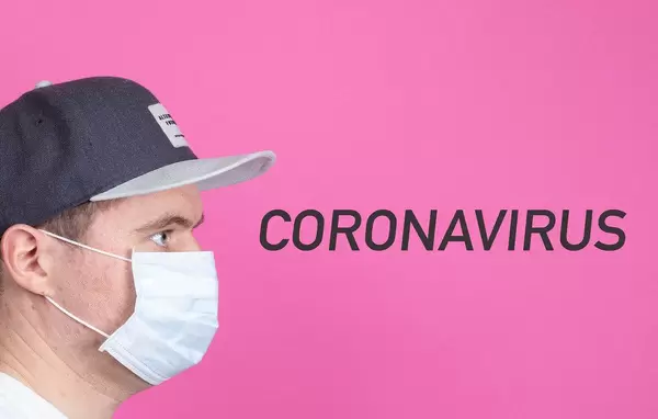 Mann mit Kappe trägt Gesichtsmaske und schaut auf das Wort Coronavirus auf pinkem Hintergrund