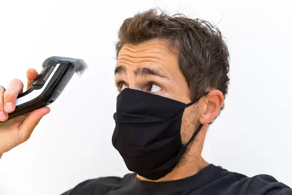 Mann mit Mundschutz schneidet sich die Haare selber: die Friseure haben in Corona-Zeiten zu