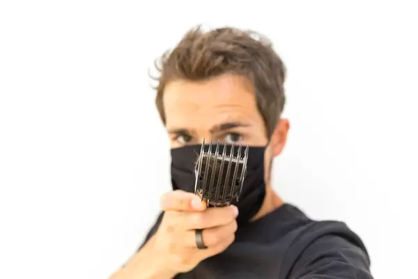 Mann mit Mundschutz zeigt den Kammaufsatz vom Philips QC5115/15 Haarschneider. Porträt vor weißem Hintergrund