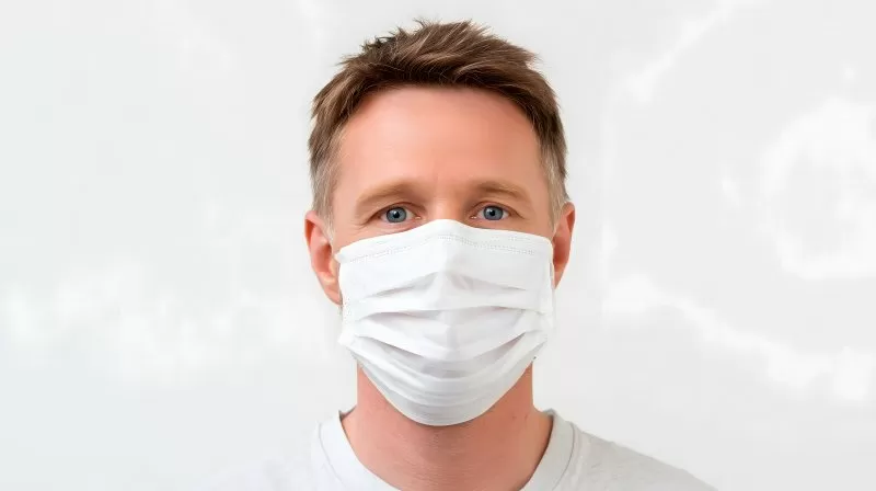 Mann mit weißer Gesichtsmaske vor hellem Hintergrund