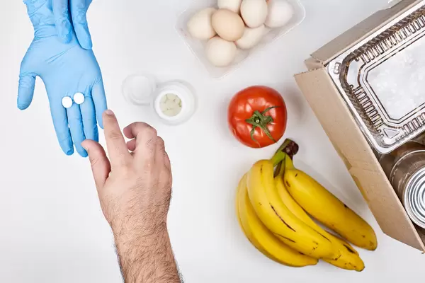 Mann nimmt Medikamente aus einer Hand mit Einweghandschuh neben Lebensmittelspende