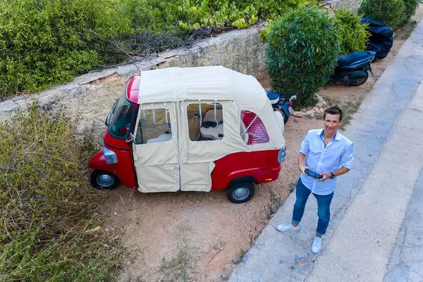Mann schießt ein Drohnen-Selbstporträt aus der Luft, vor einem witzigen Fahrzeug