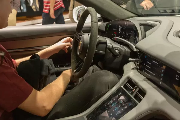 Mann sitzt im Ausstellungsfahrzeug von Porsche: E-Auto Taycan Turbo S mit Powermeter, zentraler Tempoanzeige und Touch-Bedienfeld