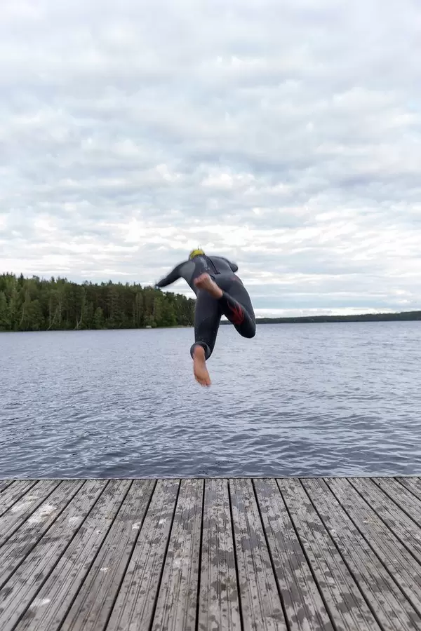 Mann springt ins Wasser durch einen großen Sprung von dem Bootssteg, um im finnischen See Päijänne schwimmen zu gehen