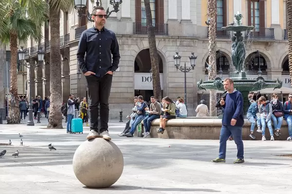 Mann steht auf einer Steinkugel neben dem Drei-Grazien-Brunnen am Placa Reial in der Katalonien-Provinz Barcelona, Spanien