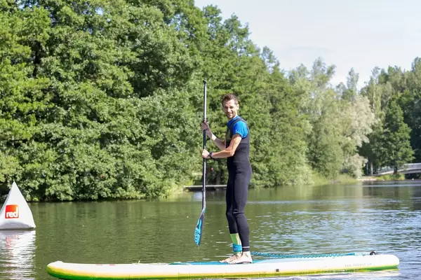 Mann steht mit Paddel auf einem Stand-Up Paddleboard und betreibt Wassersport auf einem See in Finnland