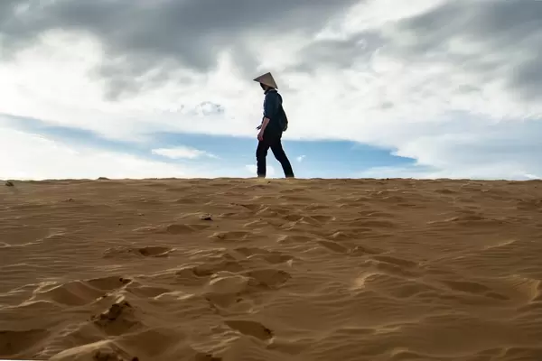 Mann steht oben auf den roten Sanddünen in Mui Ne, Vietnam vor leicht bewölktem Himmel