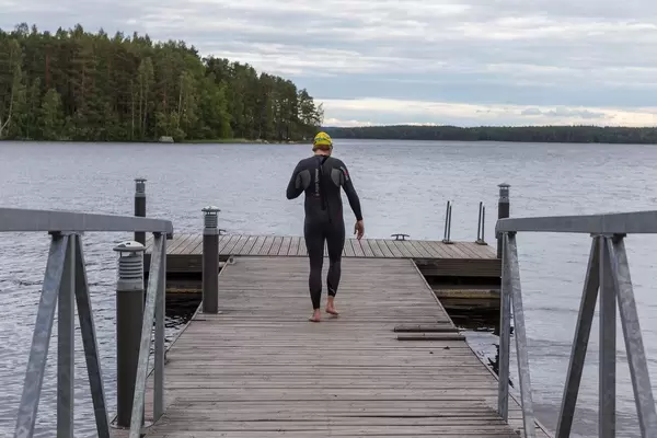 Mann von hinten mit Neoprenanzug und Tauchbrille auf einem Holzsteg am Päijännesee in Finnland