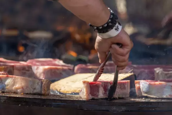 Mann wendet Kotelett auf Grillplatte mit Grillzange und trägt Armband vom Tomorrowland Festival 2019