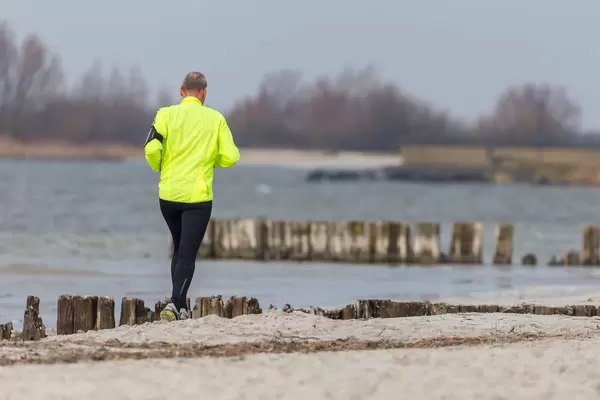Mann with reflecting yellow sports jacket running on a beach near Beach Resort Makkum
