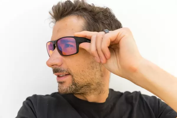 Mann zeigt seine Horus X PC Gaming Brille mit Blaulichtfilter, die die die Augen vor schädlichen Blaulichtstrahlungen schützen