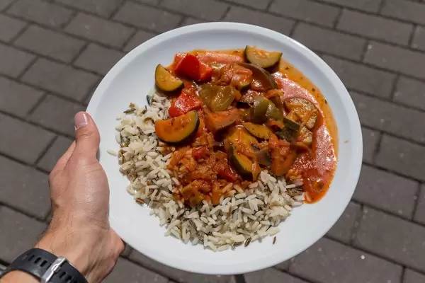 Mann zeigt veganes Ratatouille aus Zucchini, Tomaten und Zwiebeln mit Wildreis auf dem BarCamp  in Koblenz