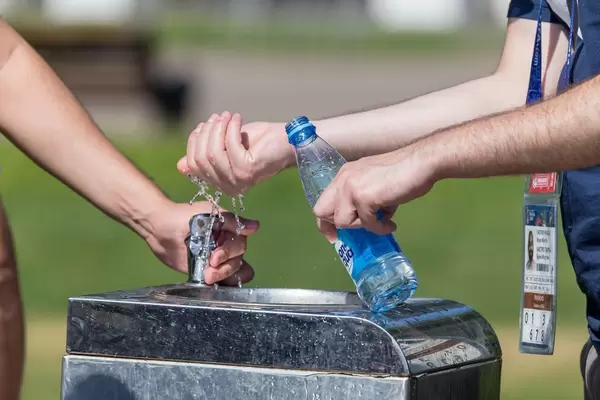 Männer befüllen am Trinkbrunnen eine Flasche mit Wasser