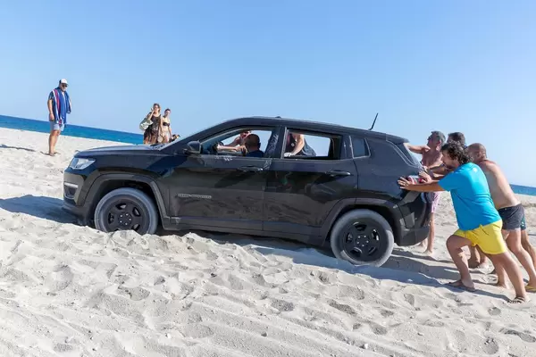 Männer schieben einen SUV auf dem Strand an