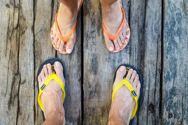 Männer- und Frauenfüße in Flip-Flops stehen sich gegenüber auf Holzboden
