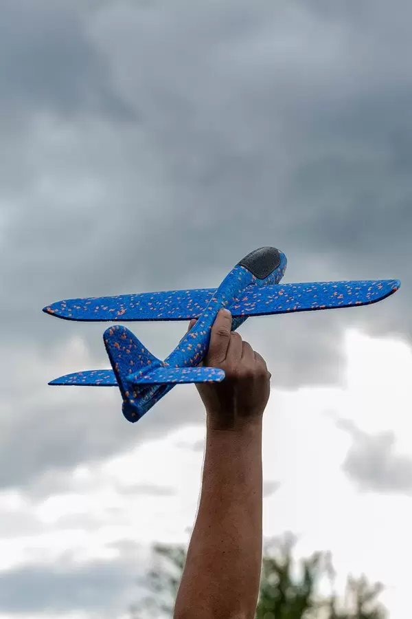 Männerhand hält ein blau-oranges Spielzeug- und Modellflugzeug in die Luft, mit dunklen Wolken im Hintergrund