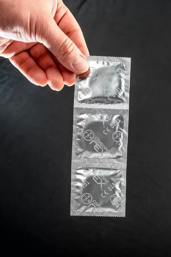 Männerhand hält einen Streifen mit verpackten Kondomen vor schwarzem Hintergrund