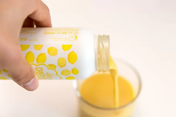 Männerhand schüttet den veganen, gelben Smoothie der True Fruits Frühlingsedition Lemon-Cheesecake in ein Glas vor weißem Hintergrund