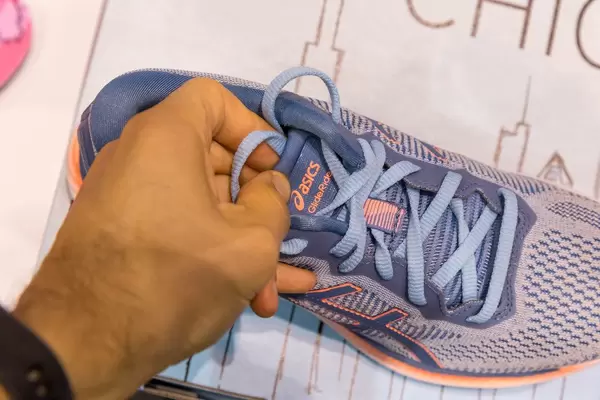 Männerhand zieht am blauen Schnürsenkel der Laufschuhe GlideRide von asics
