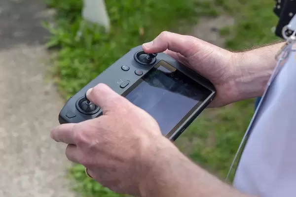 Männerhände steuern eine Drohne mit der Man operates a DJI Mavic 2 Smart Controller Fernbedienung im offenen Gelände