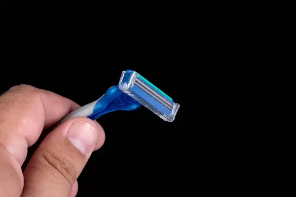 Männliche Hand hält Einwegrasierer aus Plastik mit Schutzkappe isoliert vor schwarzem Hintergrund