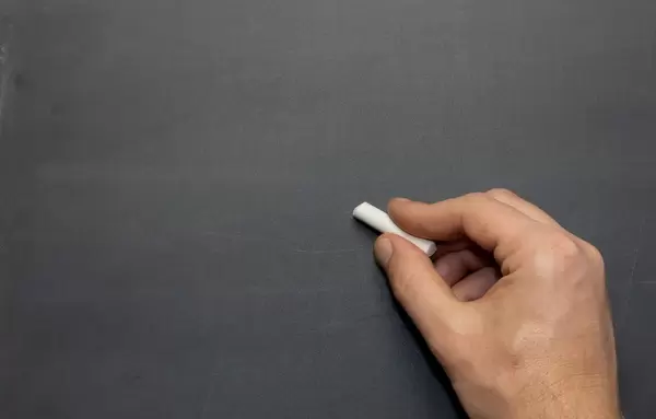 Männliche Hand mit weißem Kreidestück vor dem Beschriften einer Schultafel - Nahaufnahme frontal