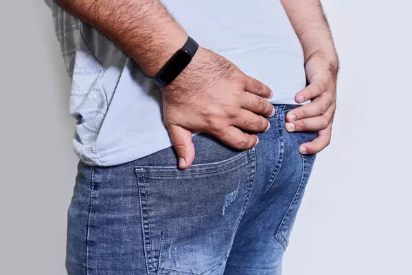 Man's hand holding his bottom because having abdominal pain and hemorrhoids - Health care concept