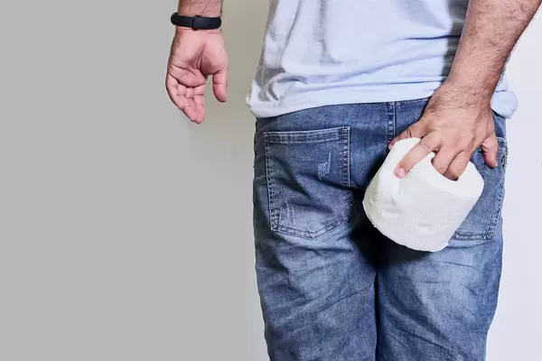 Man's hand holding toilet paper and holding his butt suffering from hemorrhoidal pain