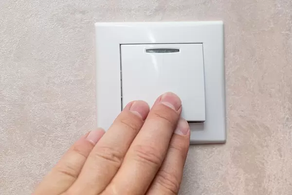 Man's hand with fingers on light switch, about to turn off the lights
