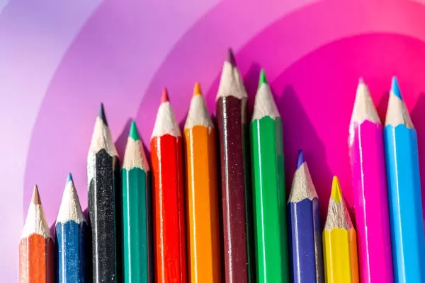 Many different colored pencils on pink background