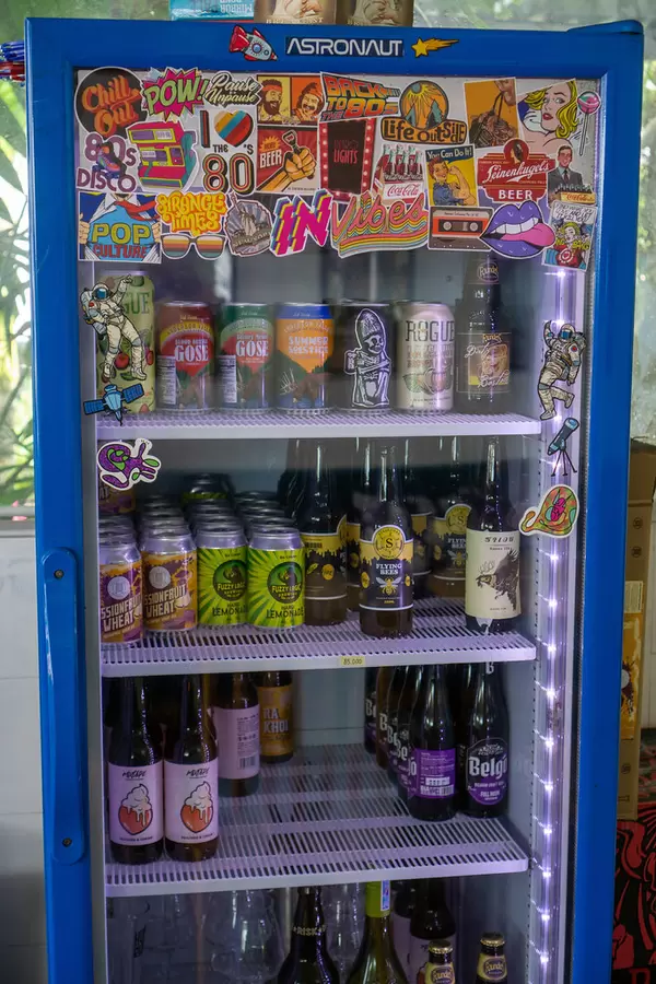 Many Retro Style Stickers on a Beverage Fridge with Beer Cans and Bottles inside it