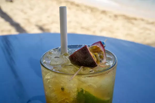 Maracuja Mojito mit Eiswürfeln, Minze, Limette und Papier-Strohhalm in einer Strandbar auf einem Holztisch Nahaufnahme