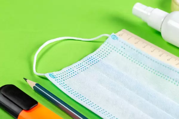 Marker, pencils, ruler, medical mask and antiseptic on a green background