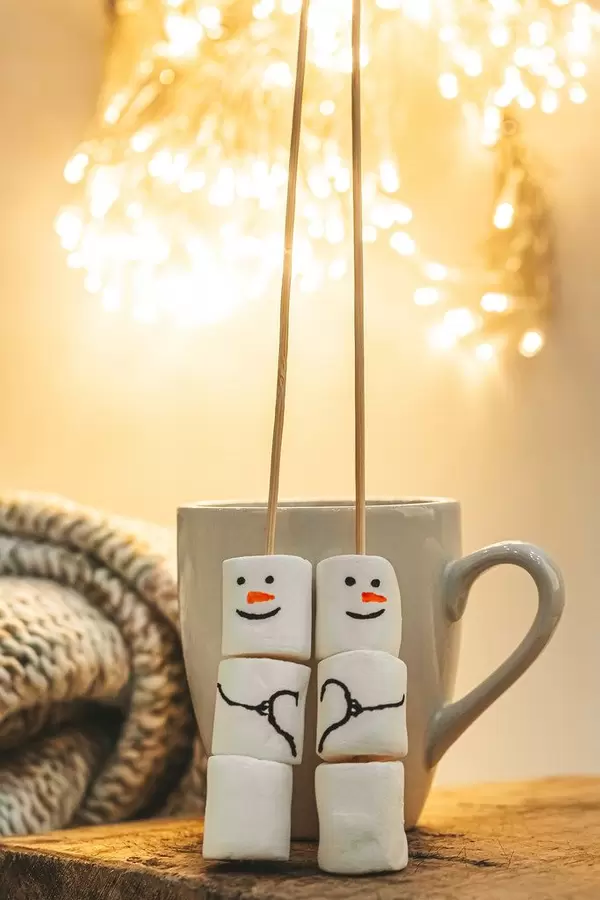 Marshmallow snowmen with a cup and beautiful bokeh of glowing garlands