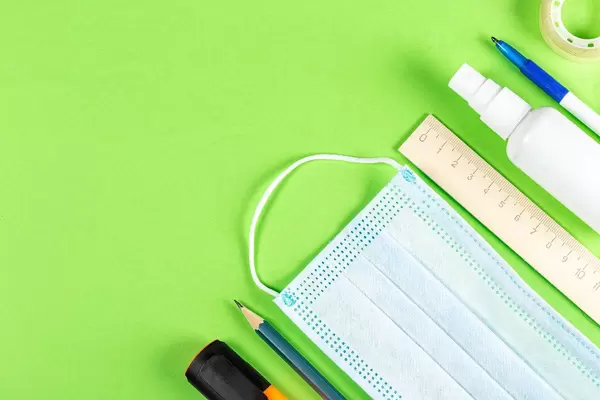 Mask and antiseptic on a green background with school supplies