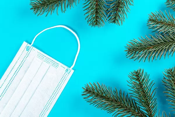 Mask and branches of a Christmas tree on a blue background with free space