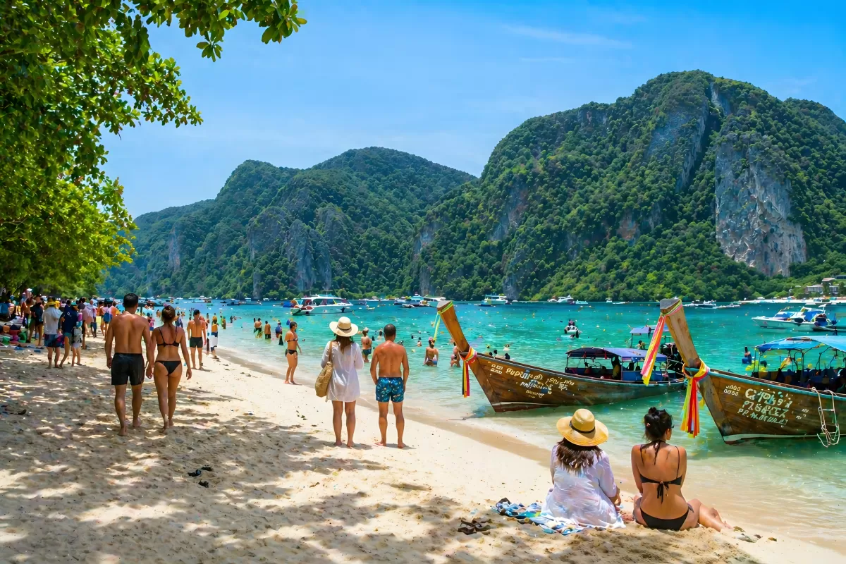 Massentourismus: Belebter Strand mit Longtail-Booten in Thailand