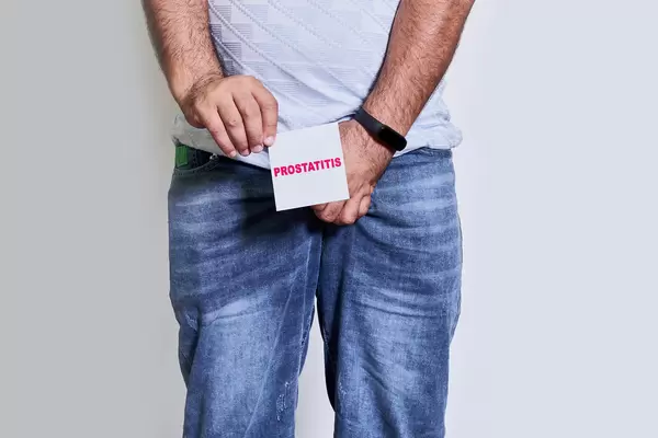 Mature man with urological problems holding a paper card with - prostatitis text over grey background