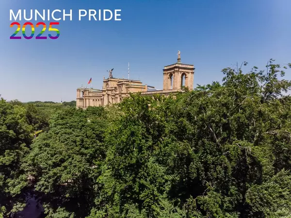 Maximilianeum behind green trees and blue sky with the picture title "Munich Pride 2025" in rainbow-colors, for the Christopher-Street-Day Festival