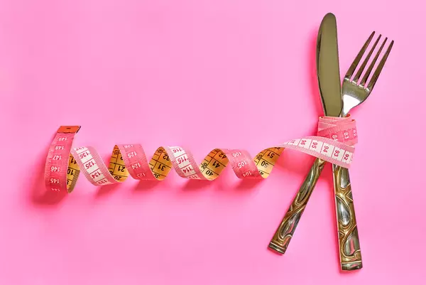 Measuring tape with spoon and fork on pink background