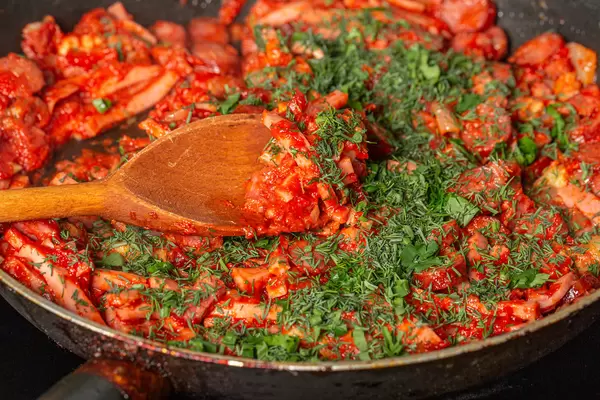 Meat and sausage cuts are fried in a frying pan with tomato sauce and herbs
