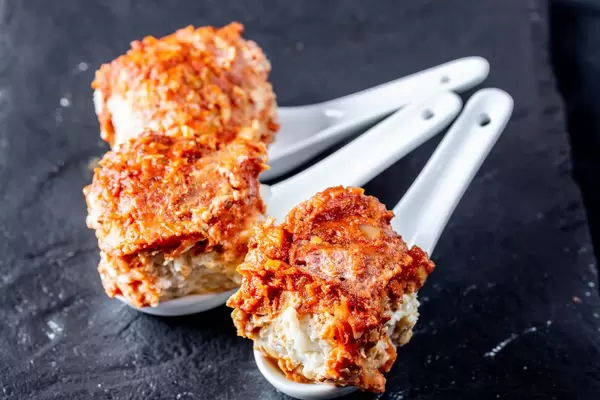 Meat balls with vegetables under red sauce served on white spoons