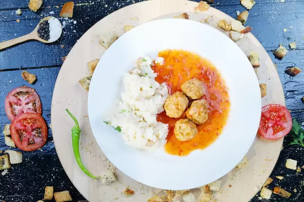 Meatballs with rice on a white plate, slices of tomatoes and hot chili (Flip 2019)