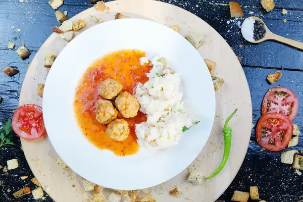 Meatballs with rice on a white plate, slices of tomatoes and hot chili