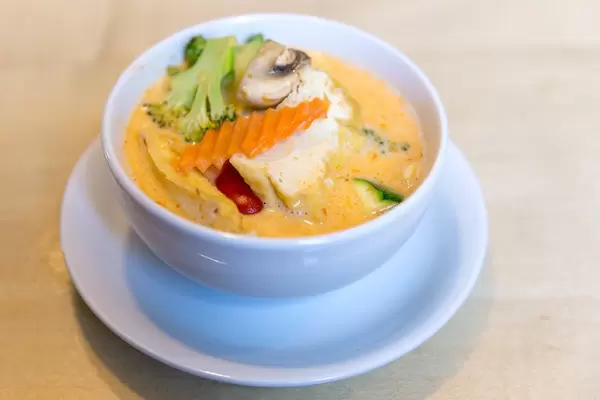 Meatless and hot spicy coconut milk soup "Tom Yum" with tofu and fresh vegetables, in a white soup bowl, as a vegan starter
