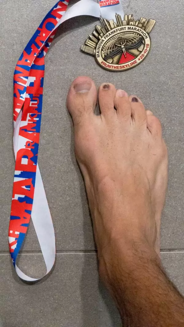 Medaille des Mainova Frankfurt Marathon 2018 auf Fliesenboden mit einem Fuß