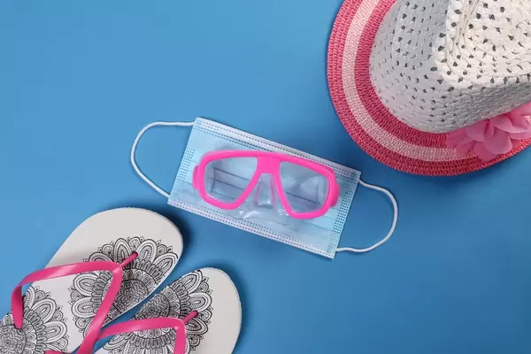 Medical face mask and diving mask with flipflops and sun hat on blue background