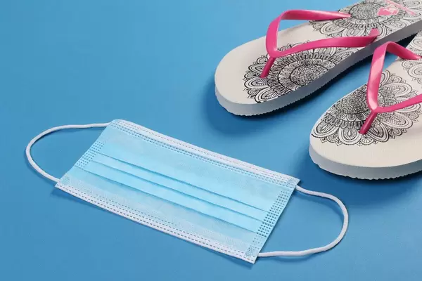 Medical face mask and flipflops on blue background