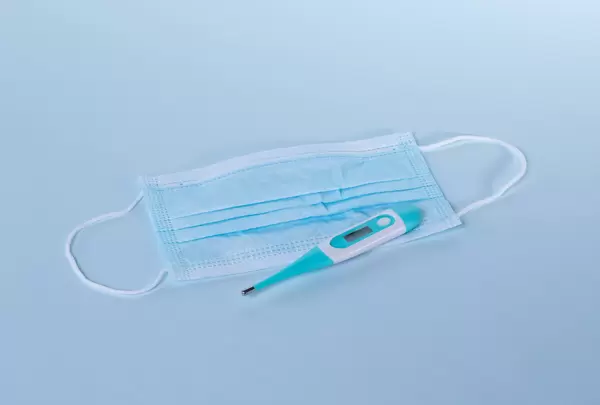 Medical face mask with digital thermometer on light blue background