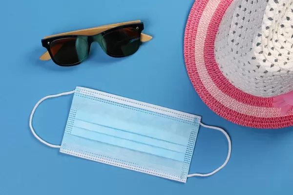 Medical face mask with sun hat and sunglasses on blue background